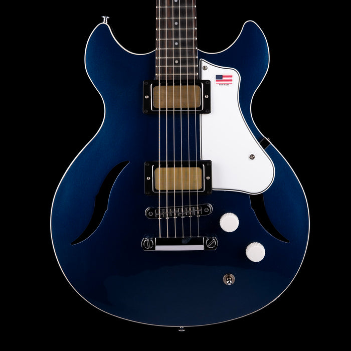 Blue electric guitar with a white pickguard on a black background