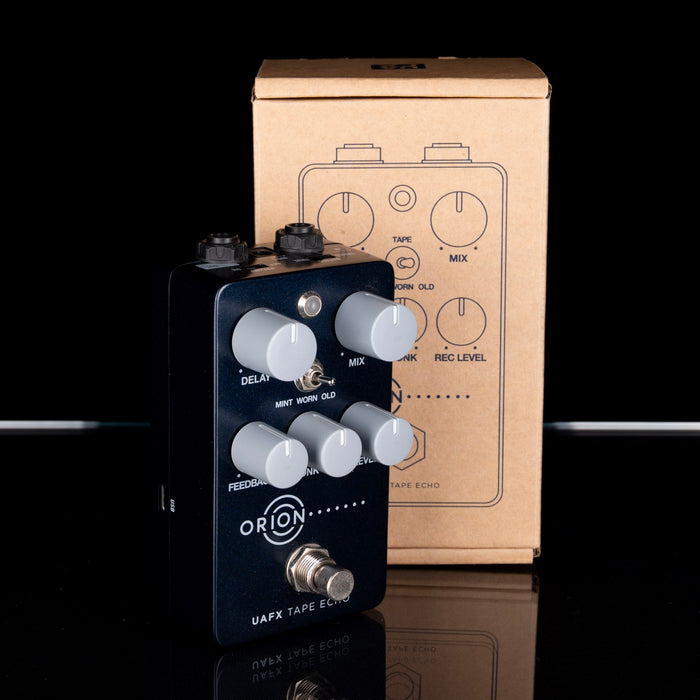 Guitar effects pedal with 'Orion' branding in front of a cardboard box with similar design elements.