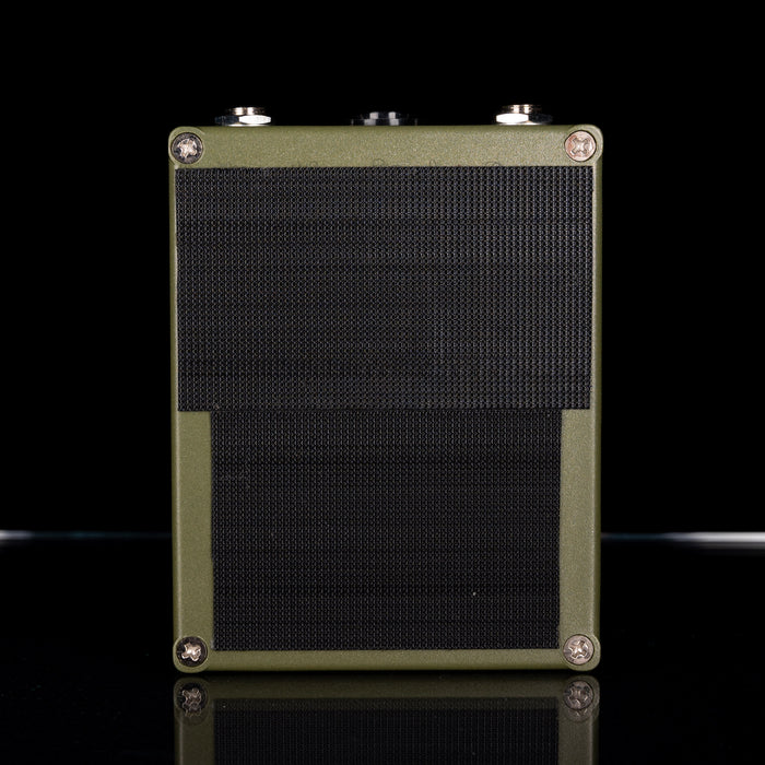 Green guitar amplifier with black mesh on a reflective surface