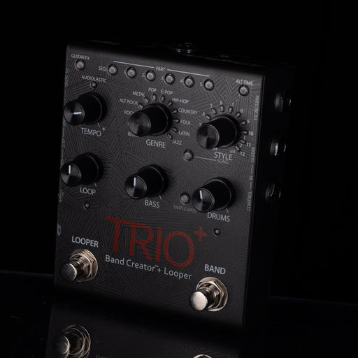 A close-up of a black Trio Band Creator+ Looper guitar effects pedal with multiple rotary knobs, switches, and foot pedals against a dark background.