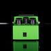 Green guitar effects pedal with black knobs on a reflective surface