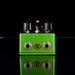 Green guitar effects pedal with multiple knobs on a black background
