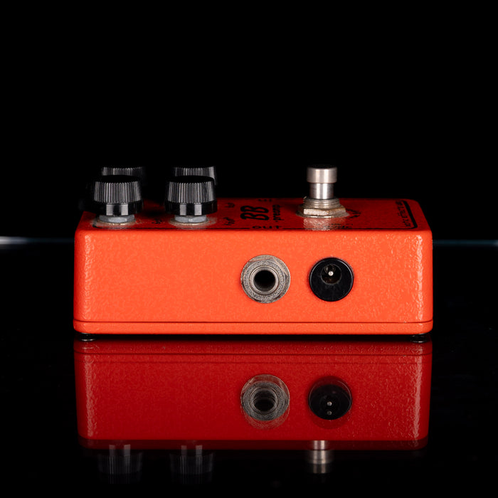 Orange guitar effects pedal with knobs and jacks on a black background