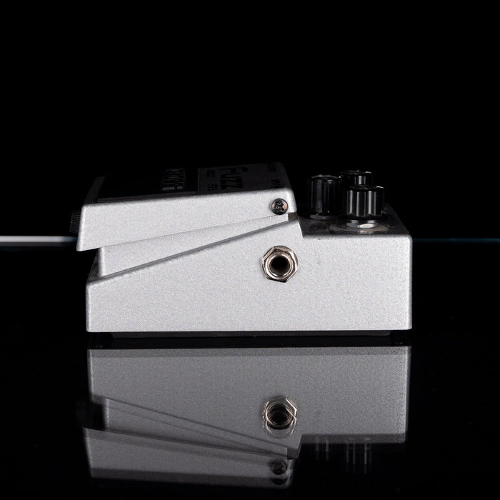 Metallic pedal with two knobs and a jack plug on a black background