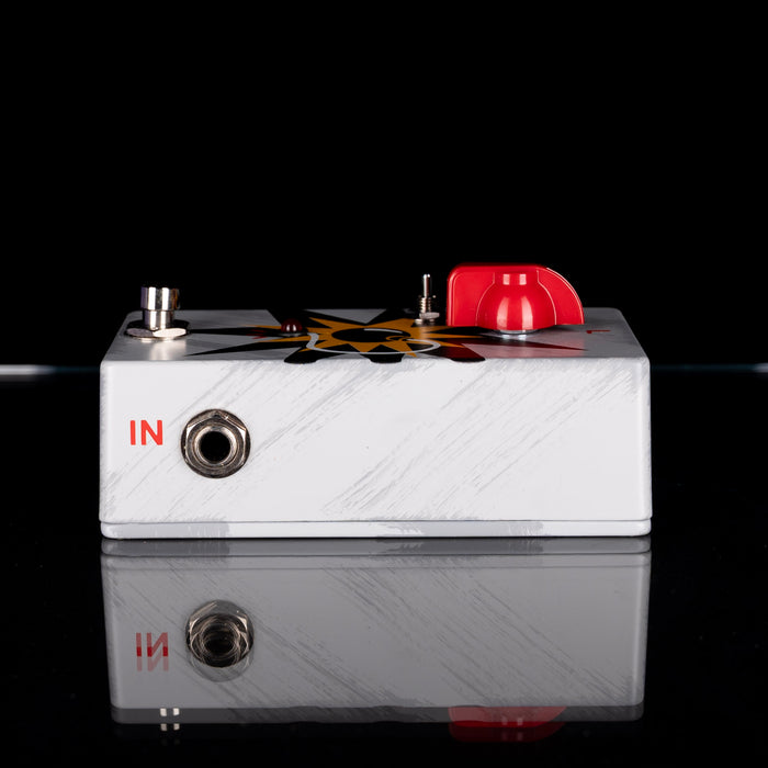 White guitar effects pedal with red and black design on a reflective surface