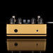 Guitar effects pedal with gold casing and black knobs on a reflective surface.