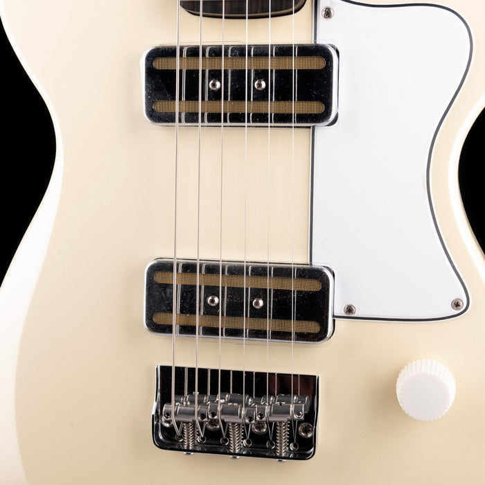 Close-up of a white electric guitar with black pickups and bridge.