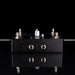 Black electronic pedal with various knobs and ports on a reflective surface with a black background