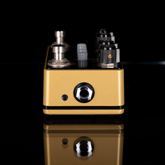 Gold and black guitar effects pedal on a reflective surface with a black background