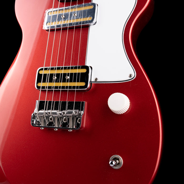 Close-up of a red electric guitar with a black pickguard on a dark background