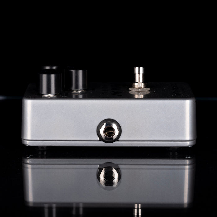 Metallic guitar effects pedal on a reflective black surface with a black background