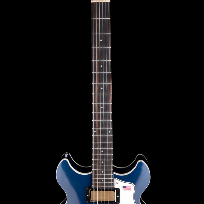 Blue electric guitar with a white pickguard on a black background